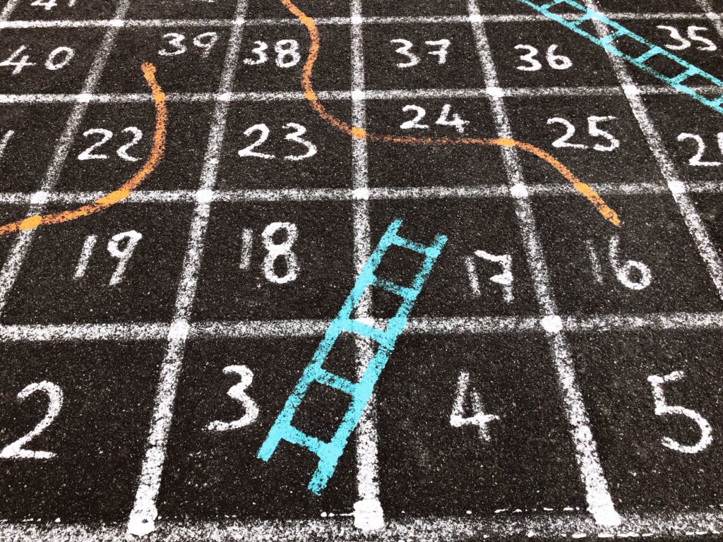 Colorful snakes and ladders game painted on a playground surface with numbered squares from 2 to 40, featuring a blue ladder and orange snake—illustrating how progress is rarely a straight line