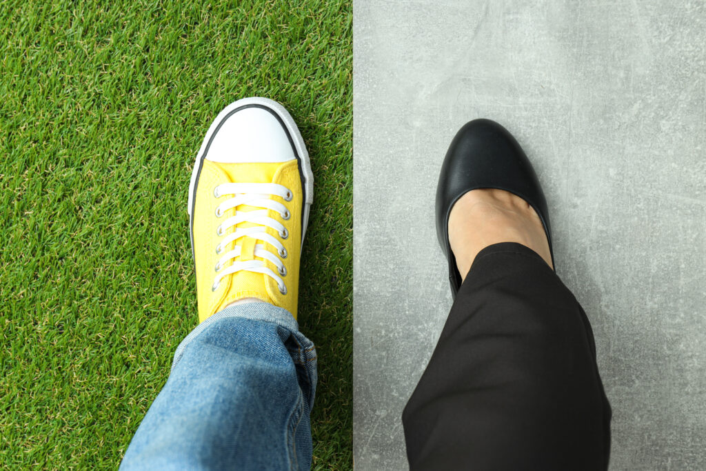 Aerial view of two feet stepping side by side — one in a yellow sneaker on grass, the other in a black dress shoe on concrete — illustrating how comparison flattens fundamentally different lives into a single measurement.