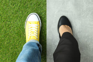 Aerial view of two feet stepping side by side — one in a yellow sneaker on grass, the other in a black dress shoe on concrete — illustrating how comparison flattens fundamentally different lives into a single measurement.