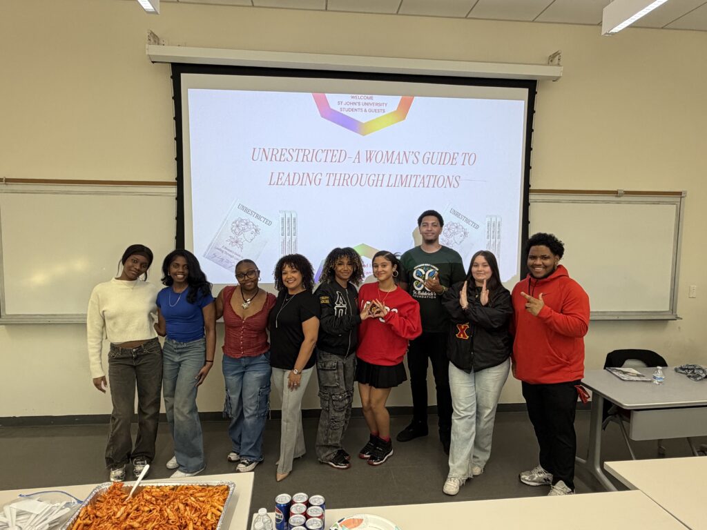Liz St. James stands with a group of students at St. John's University; the screen behind shows her book Unrestricted: A Woman's Guide to Leading Through Limitations